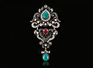 Vue détaillée d'une broche vintage de style baroque avec gemmes vertes et cristal rouge