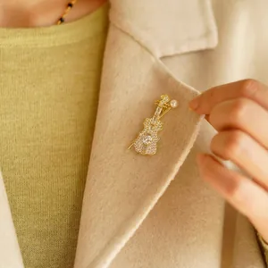 Elegant gold violin brooch with shimmering crystals and pearl on a beige wool coat