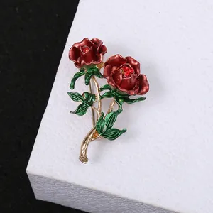 Detailed macro shot of an elegant red rose brooch with green leaves and crystal center.