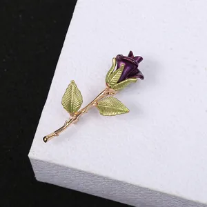 Close-up detail of an elegant purple rose brooch with green leaves and gold-tone stem
