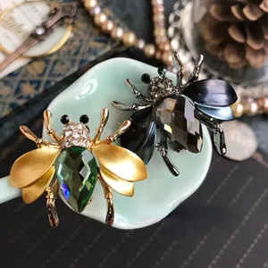 Detailopname van vintage bijenbroches in goud en zwart met facetkristallen.