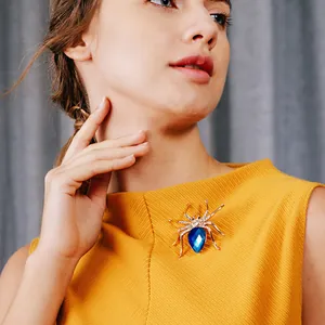 Detailaufnahme einer Vintage-Gold-Spinnenbrosche mit blauem Kristall auf gelbem Stoff