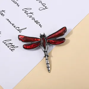 Close-up of a vintage red abalone shell dragonfly brooch on a cream background