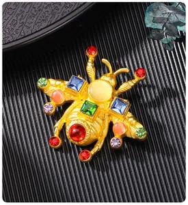 Primo piano di una spilla vintage a forma di ape dorata con vari strass multicolori.