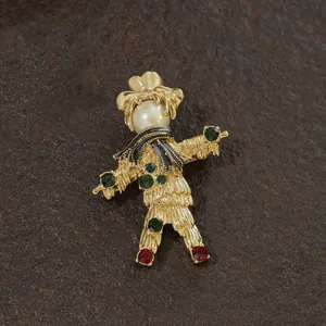 Detailed view of a vintage golden scarecrow brooch featuring a pearl head and green stones