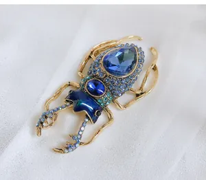 Macro view of vintage blue crystal and enamel beetle brooch on white silk fabric