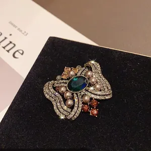 Primer plano de broche vintage con cristal verde y perlas en caja de terciopelo