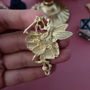 Détail macro d'une broche fée vintage en or mat avec un relief floral complexe.