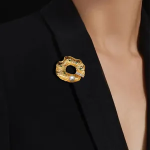 Broche dorée baroque de forme irrégulière avec perle et pierre verte sur blazer noir