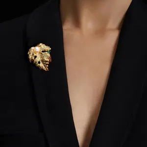 Gros plan élégant d'une broche feuille baroque dorée avec perle sur un blazer noir.