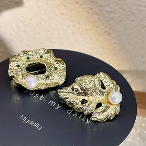 Gros plan d'une broche feuille baroque en or avec métal texturé et perle