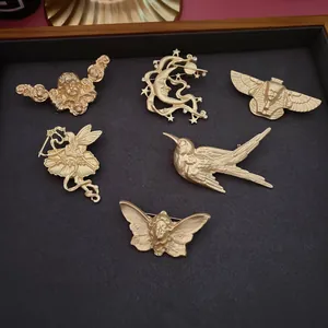 Vue détaillée de broches vintage en relief or mat avec motifs d'oiseaux et d'anges.