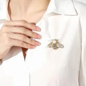 Detailed view of a sparkling crystal and pearl bee brooch pinned on a white shirt