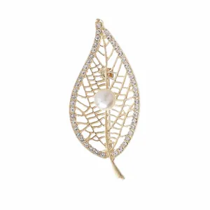 Close-up detail of a vintage gold leaf brooch featuring clear rhinestones and a central pearl