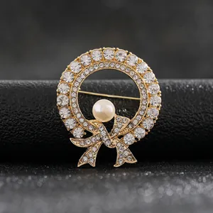 Macro view of elegant gold-toned wreath brooch with bow and central pearl detail.