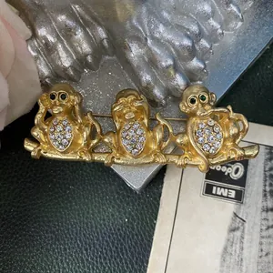 Primo piano di una spilla a forma di scimmia placcata oro vintage con tre scimmie sagge.