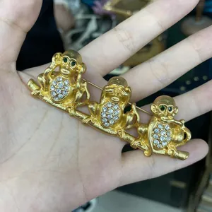 Dettaglio di una spilla placcata oro con tre scimmie della saggezza e strass.