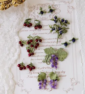 Detailed close-up of vintage grape brooches and fruit earrings on a decorative card.
