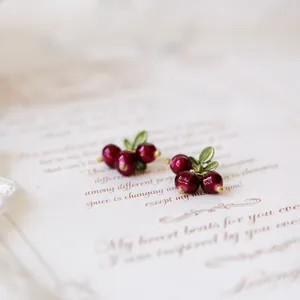 Close-up of vintage berry-shaped earrings with green leaves on a paper background