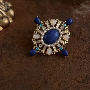 Primo piano di una spilla a croce in stile barocco con pietra blu e perle