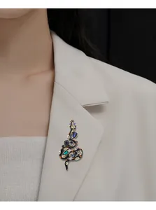 Vintage black enamel snake brooch with colorful crystals on white blazer detail view