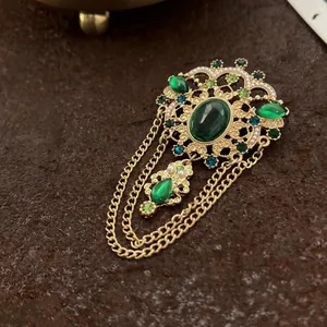Spilla barocca vintage con gemme verde smeraldo e catene dorate per abiti eleganti.