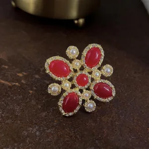 Dettaglio macro di una spilla a croce barocca vintage con pietre rosse e perle fini.
