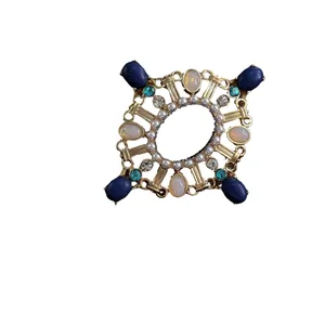 Spilla a croce barocca vintage con pietre blu e perle su sfondo bianco.