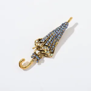 Detailansicht einer Vintage-Regenschirmbrosche mit blauen Strasssteinen und Goldfinish