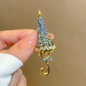 Nahaufnahme einer goldenen Vintage-Regenschirmbrosche mit blauen Kristallen in der Hand