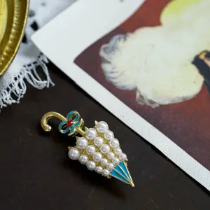 Vintage gold-plated umbrella brooch with white pearls and blue enamel bow detail.