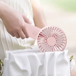 Pink portable handheld fan being placed into a white bag, compact design for summer