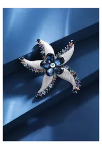 Nahaufnahme einer luxuriösen Kristall-Seestern-Brosche mit blauen und lila Steinen auf Blau.