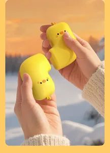 Cute yellow chick magnetic hand warmers being held in hands against a snowy winter scene.