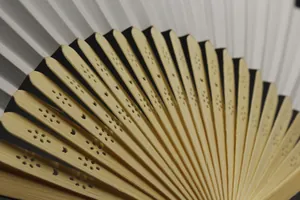 Detailed macro view of a white wedding paper fan with decorative carved bamboo ribs
