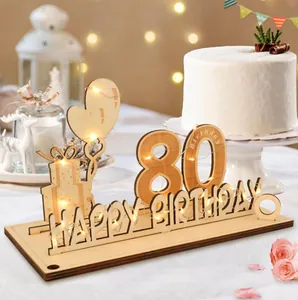 Gros plan de plaque d'anniversaire en bois 80 ans avec guirlande LED et gâteau en fond