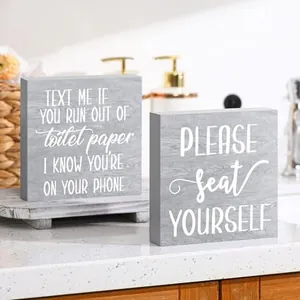Primo piano di due cartelli in legno grigio con frasi divertenti per il bagno di casa.