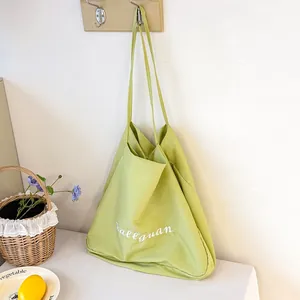Minimalist lime green canvas tote bag with white cursive embroidery hanging on a wall