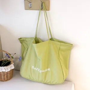 Close-up of large light green canvas tote bag with Ballguan embroidery hanging.