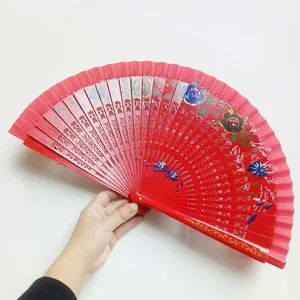 Detalle de abanico plegable español de madera roja con flores pintadas a mano y toques dorados.