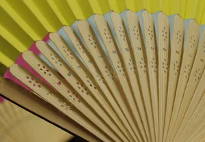 Macro detail of a yellow silk folding fan showing hollowed-out bamboo ribs texture.