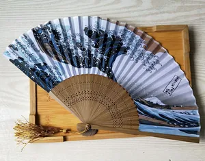 Primer plano de abanico japonés con el arte de la Gran Ola, varillas de bambú y borla dorada