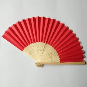 Close-up of a red silk folding fan with intricately carved bamboo ribs on plain background.