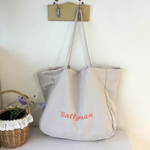 Detailed view of a minimalist large beige canvas tote bag with embroidered orange lettering