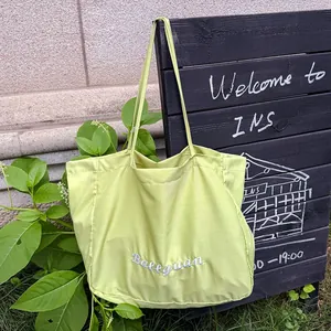 Detail of lime green tote bag with white embroidery hanging on black board.