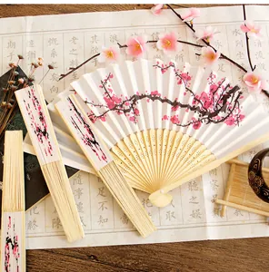 Detail view of folding bamboo fan with pink plum blossom painting on white silk fabric.