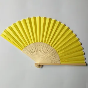 Detailed view of yellow silk folding fan with floral carvings on bamboo frame.