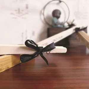 Detalle macro de un abanico de boda de madera tallada con un lazo de cinta de raso negro.