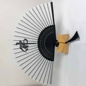 Détail d'un éventail pliant chinois de 6 pouces avec calligraphie noire et pompon élégant.