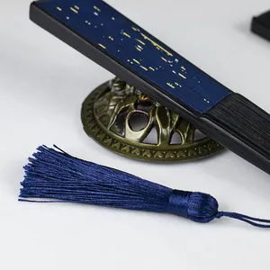 Close-up of navy blue folding fan with gold foil starry pattern and matching silk tassel